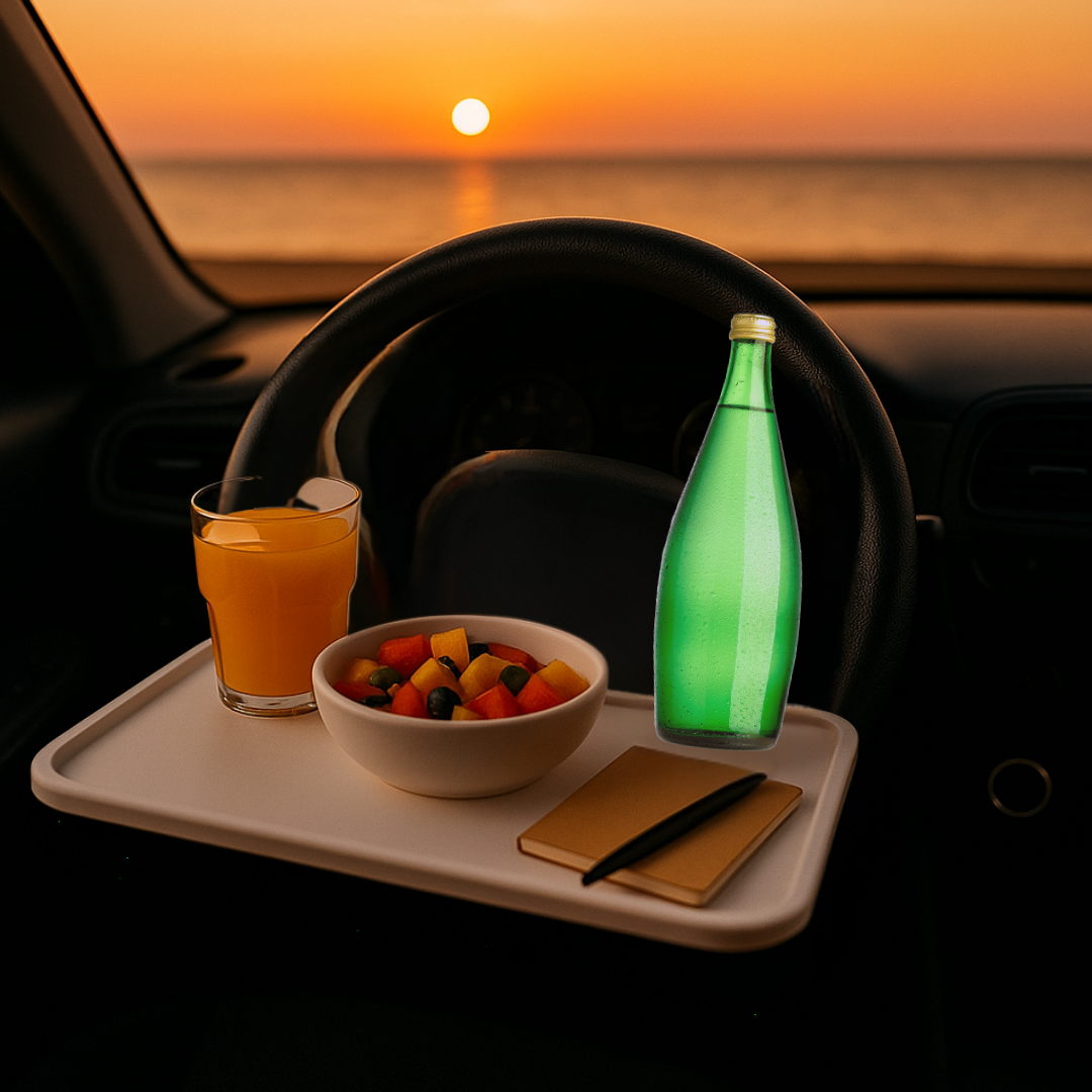 Plateau blanc accroché au volant face à la mer au coucher de soleil, salade de fruits, verre de jus d’orange, bouteille d’eau et carnet avec stylo, habitacle propre.